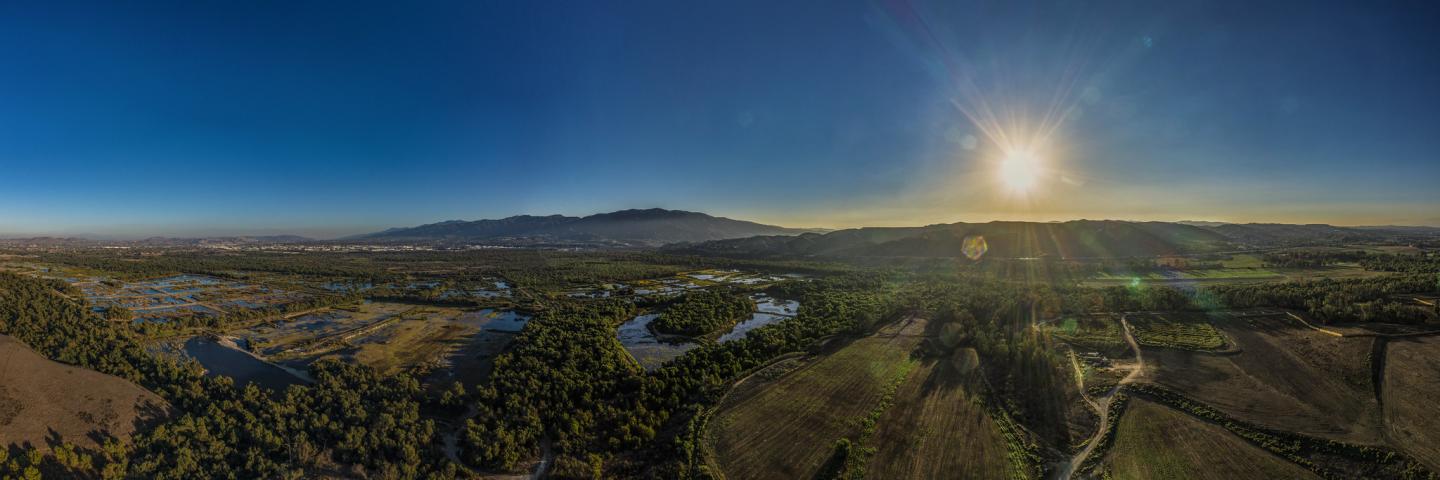 Aerial view of a landscape with multiple land uses, with blue skies and a bright sun to the right of the image.