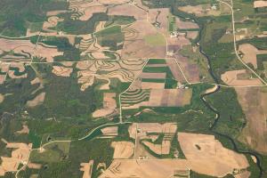 Aerial view of agricultural fields, forests, and other rural land uses, with a river running through the right side of the frame..
